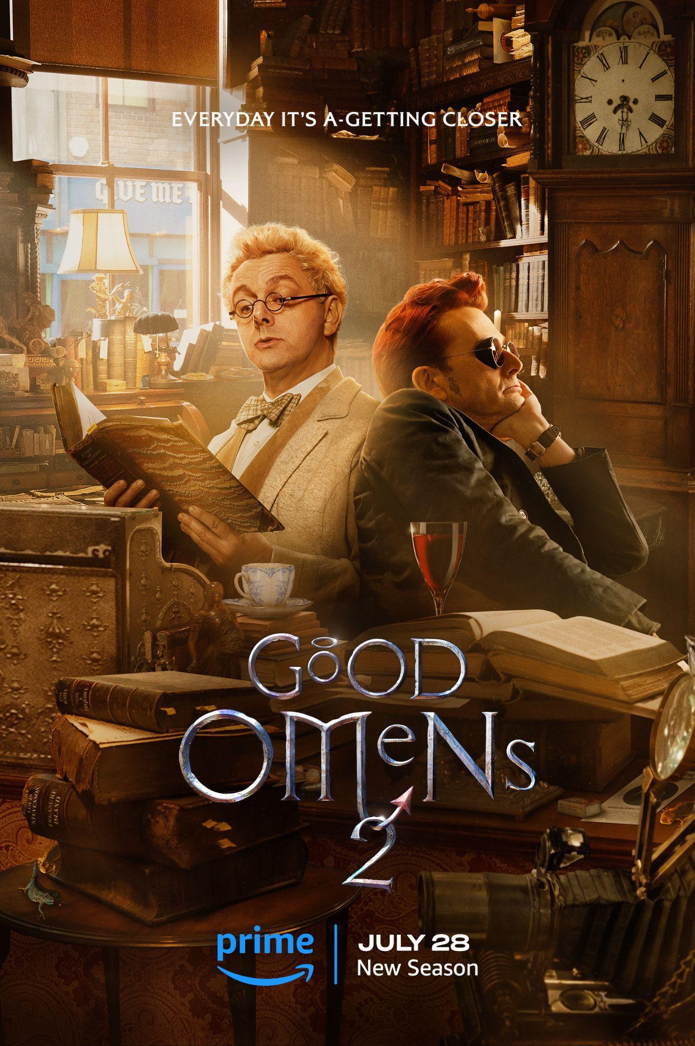 Michael Sheen dressed in white as Aziraphale holds a book, while sitting next to David Tennant dressed in black as Crowley. One has a cup of tea, the other a glass of wine.