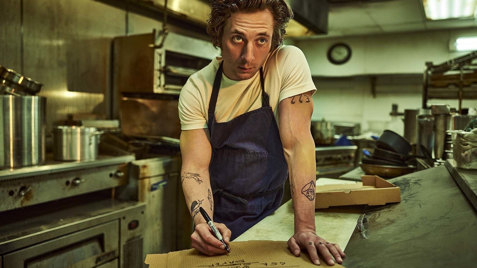 Jeremy Allen White as Carmen, standing in a kitchen writing on a piece of paper