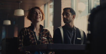 Jessie Buckley laughs, sitting next to Riz Ahmed on a bus