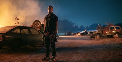 Anthony Mackie as John Doe stands by a burning car